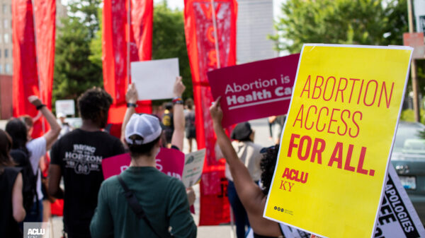 Protesters hold signs at rally in Louisville, KY. Yellow poster on right half reads, "Abortion access for all." Other signs are illegible.
