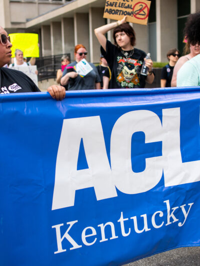 Two people carrying a blue ACLU of Kentucky banner during a march in streets in downtown Louisville KY