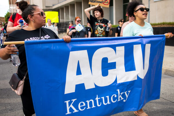 Two people carrying a blue ACLU of Kentucky banner during a march in streets in downtown Louisville KY