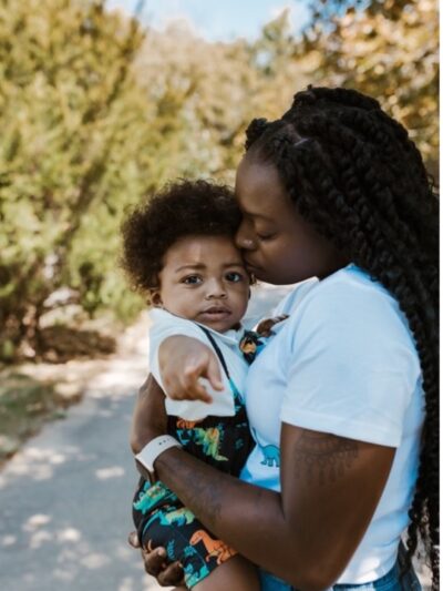 Katima holds her son, Mylo, as Mylo points to the camera and Katima kisses his forehead.