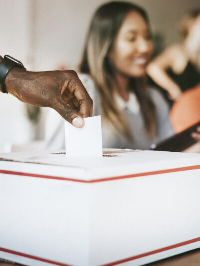 A Black hand inserts a ballot into a voting box.