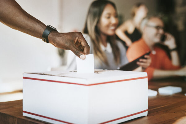 A Black hand inserts a ballot into a voting box.