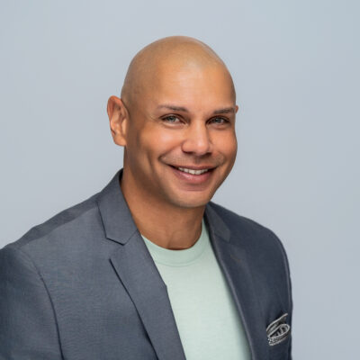Smiling Black man in light green shirt and grey jacket.