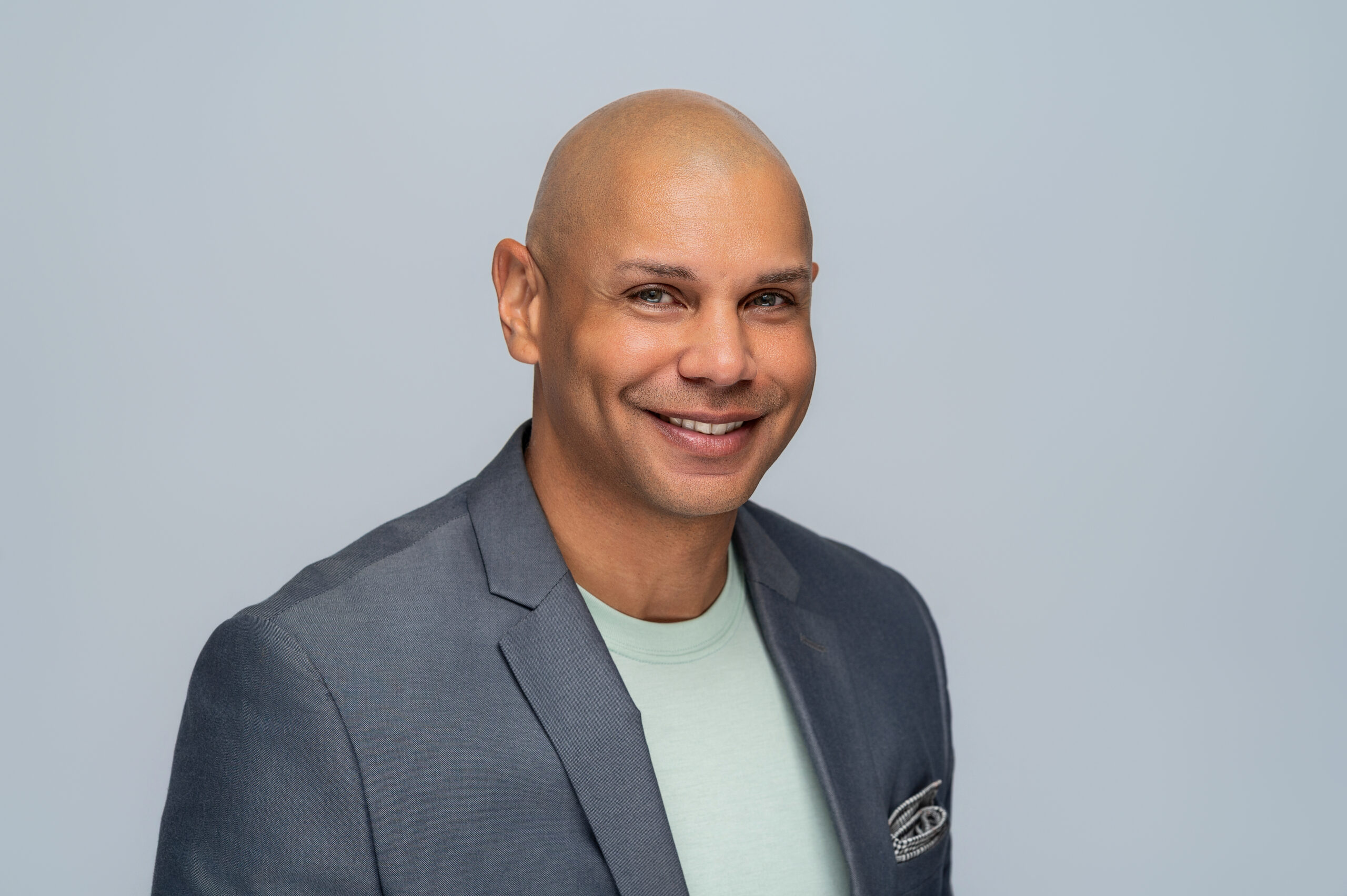 Smiling Black man in light green shirt and grey jacket.
