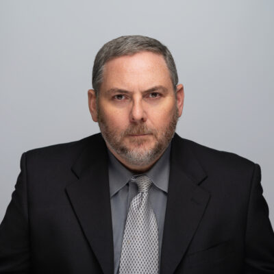 bill sharp, stern to camera, wearing a black suit coat and a grey shirt and tie