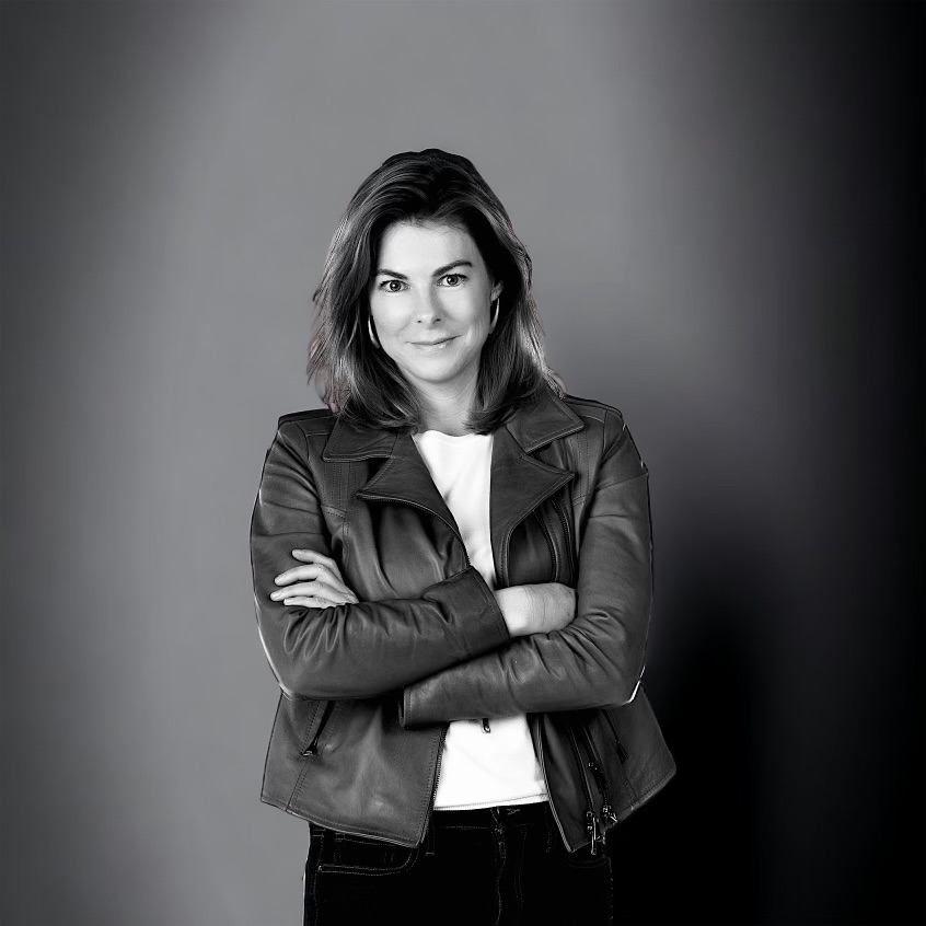 black and white photo of katherine paisley. she's standing with her arms crossed wearing a leather jacket