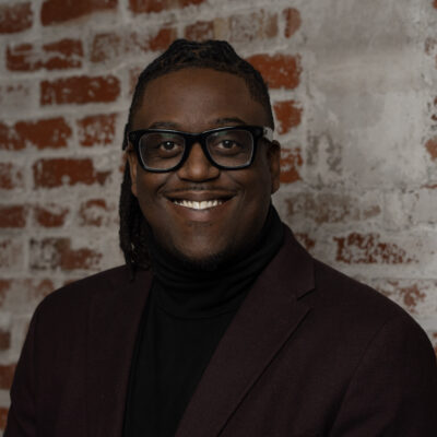 stephon smiles with glasses and a suit coat
