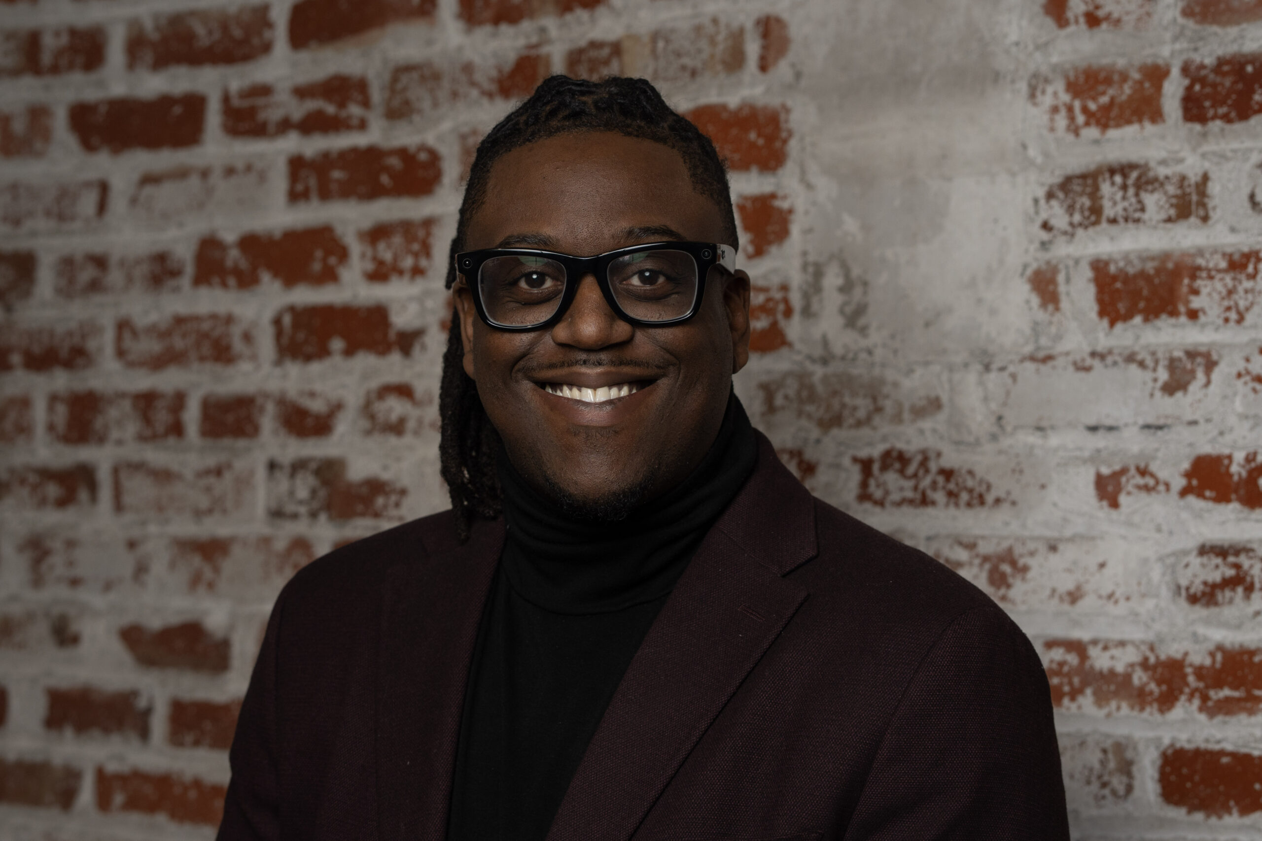 stephon smiles with glasses and a suit coat