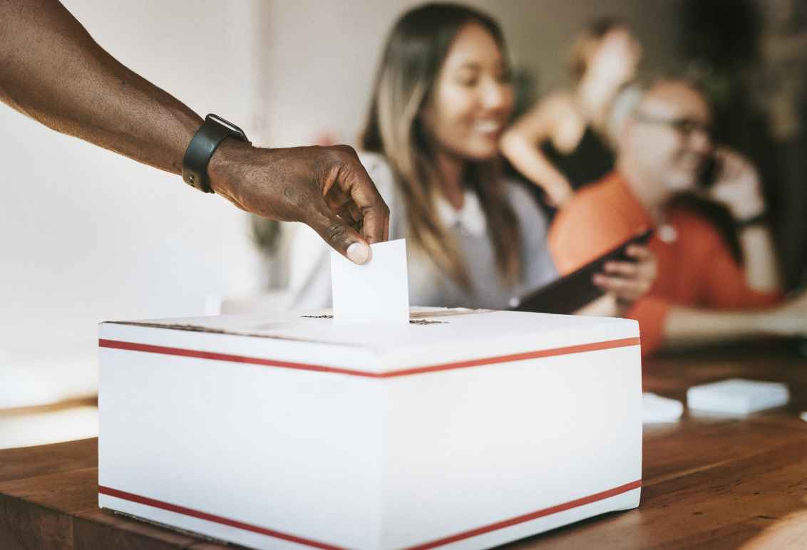 A Black hand inserts a ballot into a voting box.
