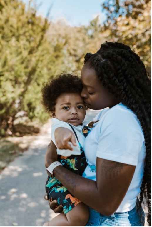 Katima holds her son, Mylo, as Mylo points to the camera and Katima kisses his forehead.