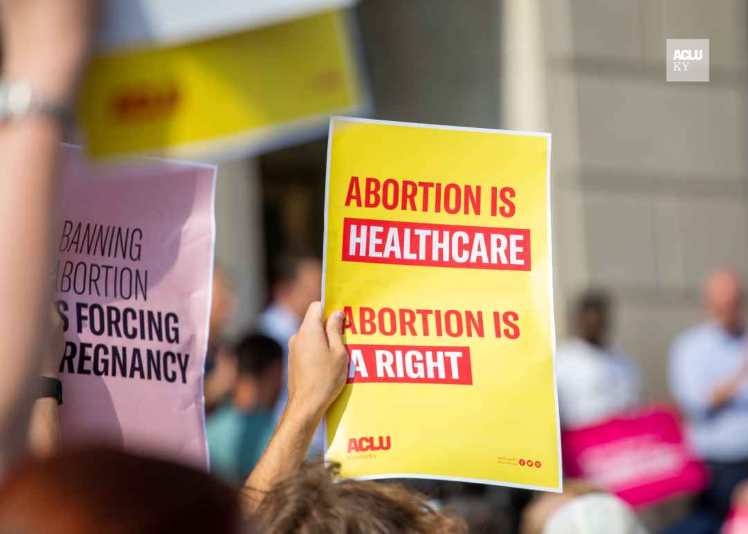 Person holding yellow protest sign that reads "Abortion is Healthcare. Abortion is a right."