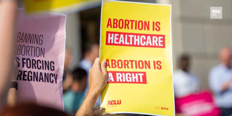 Person holding yellow protest sign that reads "Abortion is Healthcare. Abortion is a right."