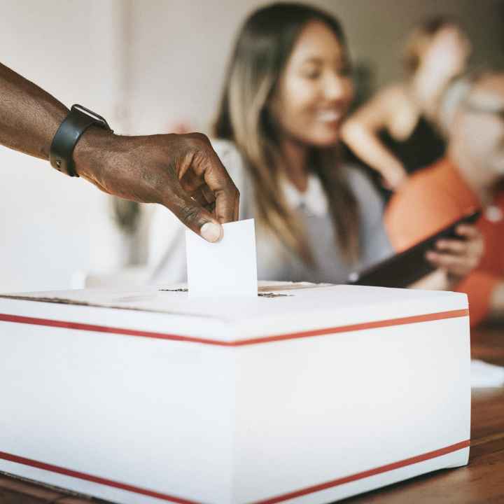 A Black hand inserts a ballot into a voting box.