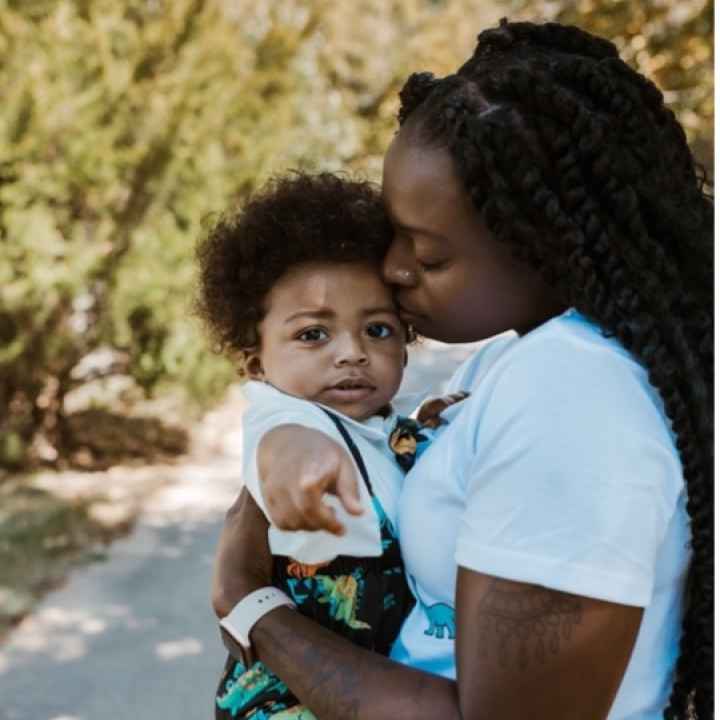 Katima holds her son, Mylo, as Mylo points to the camera and Katima kisses his forehead.