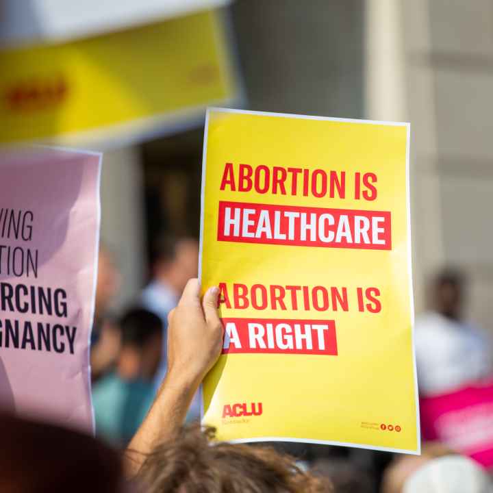 Person holding yellow protest sign that reads "Abortion is Healthcare. Abortion is a right."